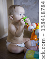 Caucasian Baby Mouthing Green Teether While Seated, Strong Chewing Motion Visible, Bright Home Backdrop, Candid Moment Of Sensory Play And Early Oral Development verical 138418784