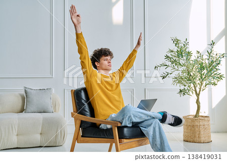 Young man with laptop in chair, stretching raising his arms, during break from work Young man with laptop in chair, stretching raising his arms, during break from work 138419031