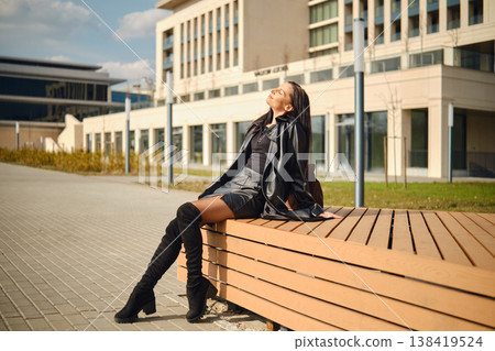 Model relaxes on a bench outside a modern building during a sunny afternoon Model relaxes on a bench outside a modern building during a sunny afternoon 138419524