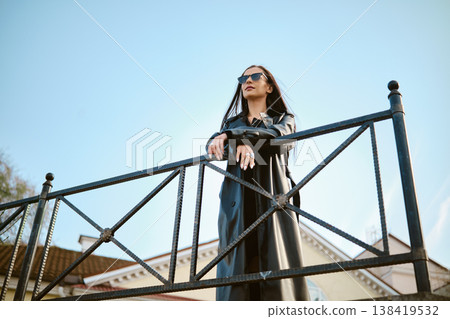 Woman in sunglasses stands on a metal railing looking at the sky during daytime 138419532