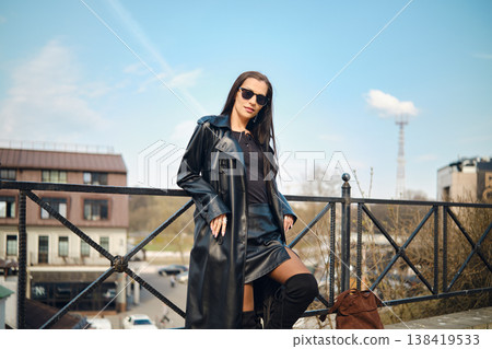 Woman in black outfit stands by railing in city under clear blue sky at daytime 138419533