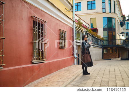 Woman stands on street in urban area while using phone during daylight in a quiet moment 138419535