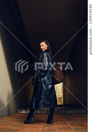 Woman walking in a dark hallway wearing a long coat with a bag in her hand during daylight hours Woman walking in a dark hallway wearing a long coat with a bag in her hand during daylight hours 138419540