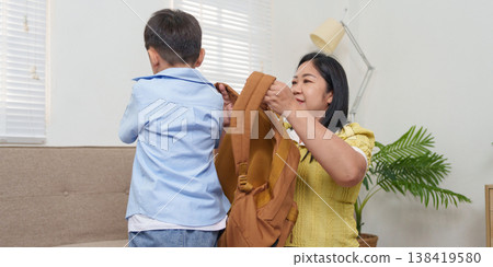 Mother helping her child put on a backpack at home Mother helping her child put on a backpack at home 138419580