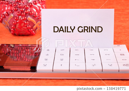 A white card with daily grind inscribed stands poised on a sleek calculator, reflecting the start of a busy work day 138419771