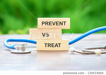 Three wooden blocks clearly spelling Prevent vs Treat are stacked beside a blue stethoscope on a textured wooden table, framed by a soft green natural backdrop 138419884