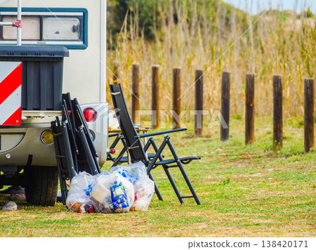 Camper vehicle camping on nature with camp chairs outside and many trash bags 138420171