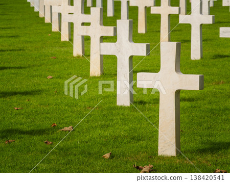 Graves with white crosses arranged in rows on green grass in a memorial cemetery during daylight hours Graves with white crosses arranged in rows on green grass in a memorial cemetery during daylight hours 138420541