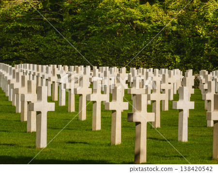 Graves with white crosses arranged in rows on green grass in a memorial cemetery during daylight hours 138420542