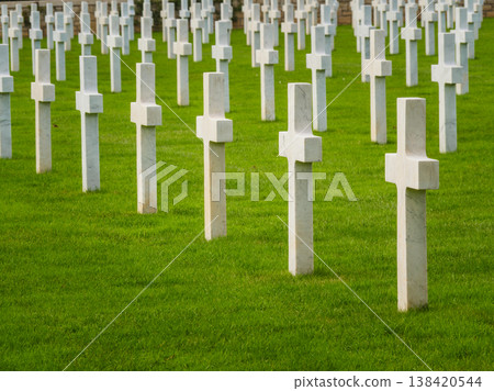 Graves with white crosses arranged in rows on green grass in a memorial cemetery during daylight hours 138420544