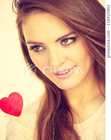 Flirty woman holding red wooden heart on stick Flirty woman holding red wooden heart on stick 138420902