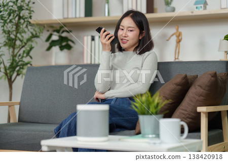 Woman speaking to smart speaker in a cozy living room Woman speaking to smart speaker in a cozy living room 138420918