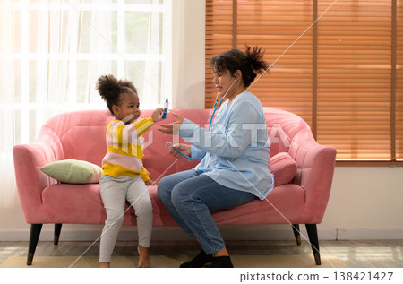 African child and curly hair mother playing doctor on pink sofa in living room at home African child and curly hair mother playing doctor on pink sofa in living room at home 138421427