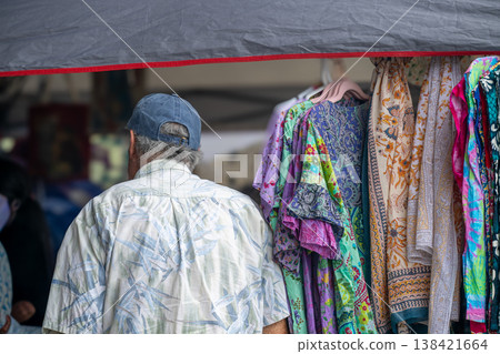 Man walks past colorful clothing at local market during afternoon hours in a warm setting Man walks past colorful clothing at local market during afternoon hours in a warm setting 138421664