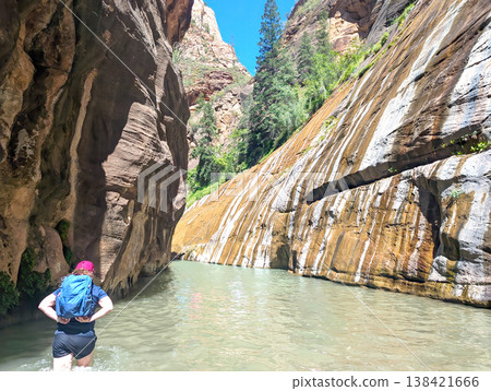 A single hiker lifting a pack as she begins a deep section of the Narrows in Zion National Park A single hiker lifting a pack as she begins a deep section of the Narrows in Zion National Park 138421666