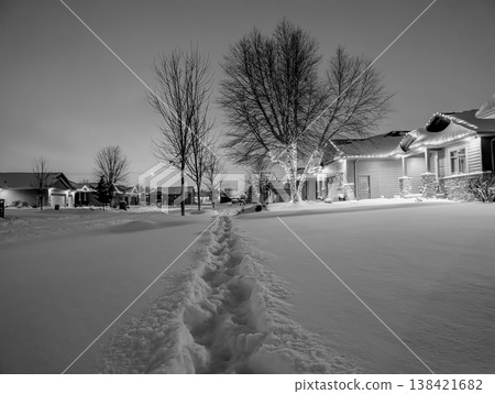 Snow covers a suburban neighborhood at night with footprints leading through the white blanket 138421682