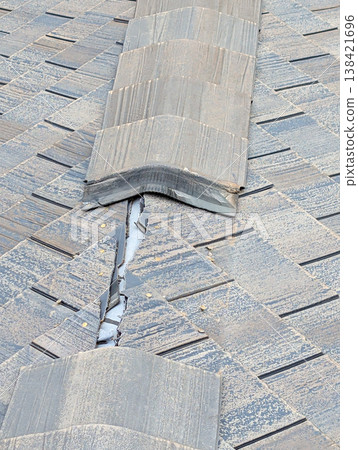 Close view of broken shingles on a roof showing cracks and wear in an urban setting during daytime Close view of broken shingles on a roof showing cracks and wear in an urban setting during daytime 138421696