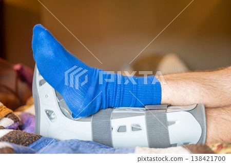 Foot in a medical boot rests on a bed with blankets during recovery at home after an injury Foot in a medical boot rests on a bed with blankets during recovery at home after an injury 138421700
