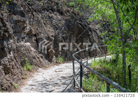 Scenic pathway winding through rocky terrain with lush vegetation under clear skies at Diamond Head State Monument Scenic pathway winding through rocky terrain with lush vegetation under clear skies at Diamond Head State Monument 138421728