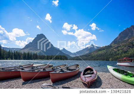 Canoes lined up on a serene lakeshore under a bright blue sky in the mountains 138421828