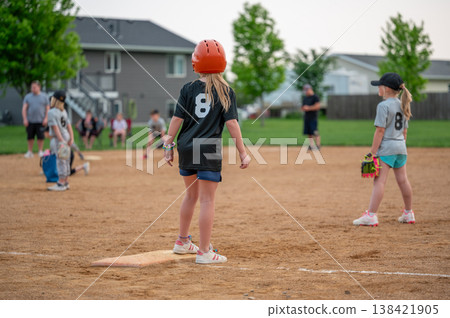 Children play softball at a community park with a game happening in the evening after school in suburbia Children play softball at a community park with a game happening in the evening after school in suburbia 138421905