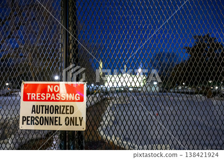Nighttime view of a fenced area with a no trespassing sign in a city environment near a building lit by lights Nighttime view of a fenced area with a no trespassing sign in a city environment near a building lit by lights 138421924