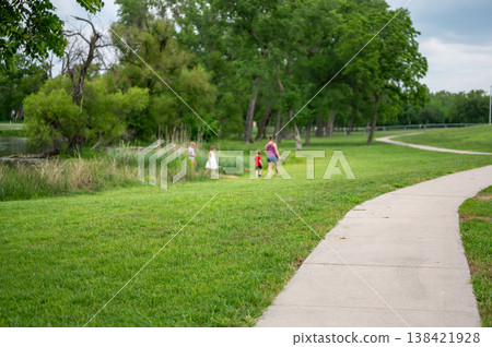 Children walk by the water while adults stay on the path in a park during a cloudy day in summer Children walk by the water while adults stay on the path in a park during a cloudy day in summer 138421928