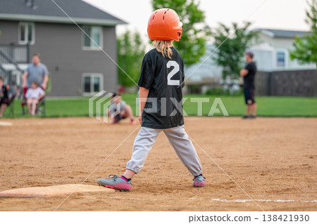 Child playing baseball on a field during a game in a neighborhood park in the evening with teammates and spectators present Child playing baseball on a field during a game in a neighborhood park in the evening with teammates and spectators present 138421930