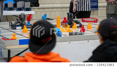 Teams compete in a robot challenge on a game table with colored blocks during a robotics event in a school gym Teams compete in a robot challenge on a game table with colored blocks during a robotics event in a school gym 138421963
