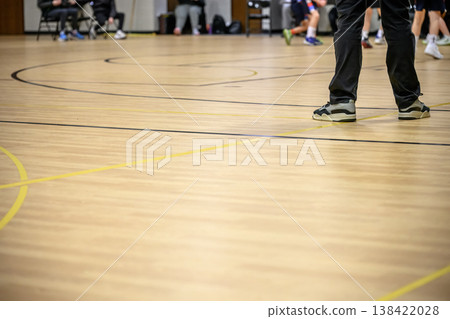Players practice basketball on a gym court while coaches observe the activity from the sidelines during evening training session Players practice basketball on a gym court while coaches observe the activity from the sidelines during evening training session 138422028