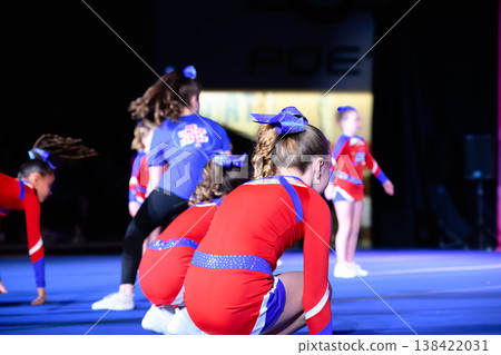 Cheerleading performance with young athletes in red outfits during event at indoor arena in evening Cheerleading performance with young athletes in red outfits during event at indoor arena in evening 138422031