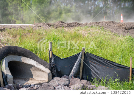 Construction site showing drainage work with black fabric barriers in green grassy area near roadway during daytime 138422035