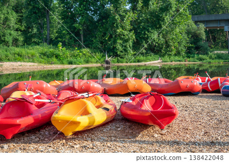 People prepare for kayaking on a warm sunny day at a river with red and yellow kayaks lined up on the shore People prepare for kayaking on a warm sunny day at a river with red and yellow kayaks lined up on the shore 138422048
