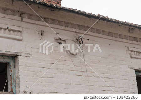 Weathered White Brick Building Exterior With Exposed Wires And Cracks Showing Signs Of Aging And Neglect In A Rural Setting Weathered White Brick Building Exterior With Exposed Wires And Cracks Showing Signs Of Aging And Neglect In A Rural Setting 138422266