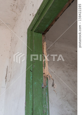 Weathered Green Wooden Door Frame With Peeling Paint Exposed Raw Wood And Cracked White Plastered Wall Background Showing Decay Weathered Green Wooden Door Frame With Peeling Paint Exposed Raw Wood And Cracked White Plastered Wall Background Showing Decay 138422285