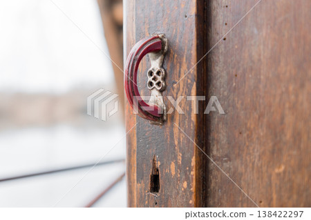 Vintage Red Door Handle Close-Up on Weathered Wooden Surface With Snowy Winter Background Blurred Outdoors Scene Capturing Rustic Charm And Textured Details 138422297