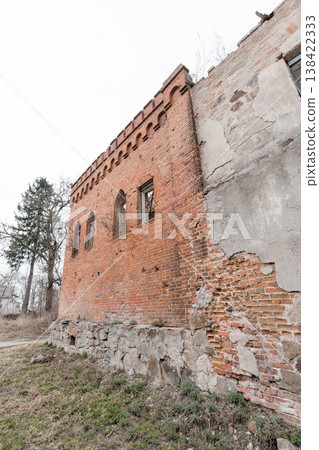 Weathered Red Brick Ruin With Gothic Arched Windows And Crumbling Stone Foundation In Overgrown Rural Landscape Under Gray Sky Weathered Red Brick Ruin With Gothic Arched Windows And Crumbling Stone Foundation In Overgrown Rural Landscape Under Gray Sky 138422333