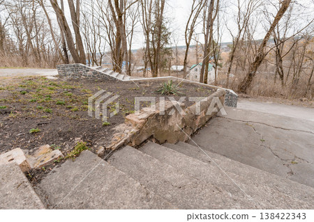 Weathered Concrete Steps Leading Up to Stone Retaining Wall Amidst Bare Trees and Distant Rural Houses in Overcast Natural Setting with Earthy Tones and Textured Surfaces Weathered Concrete Steps Leading Up to Stone Retaining Wall Amidst Bare Trees and Distant Rural Houses in Overcast Natural Setting with Earthy Tones and Textured Surfaces 138422343