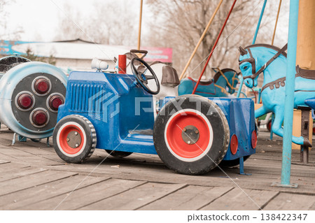 Vintage Blue Tractor and Carousel Horse Ride at Outdoor Amusement Park With Wooden Platform and Retro Color Palette Vintage Blue Tractor and Carousel Horse Ride at Outdoor Amusement Park With Wooden Platform and Retro Color Palette 138422347