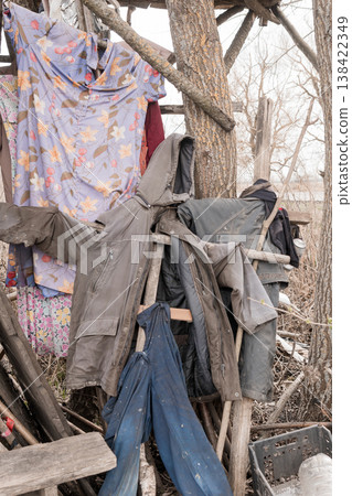 Weathered Clothes Hanging on Rustic Wooden Structure Amidst Bare Trees in Overcast Outdoor Setting Featuring Floral Shirt and Denim Pants with Earthy Tones Weathered Clothes Hanging on Rustic Wooden Structure Amidst Bare Trees in Overcast Outdoor Setting Featuring Floral Shirt and Denim Pants with Earthy Tones 138422349