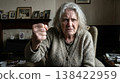 A portrait of an elderly woman with grey hair sitting in an armchair, looking directly at the camera with an angry expression and holding up a clenched fist 138422959