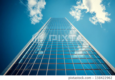 Looking up at a modern glass skyscraper against a blue sky with clouds. Low angle view of a corporate office building reflecting the sky. Business, success, and future architecture concept 138422962
