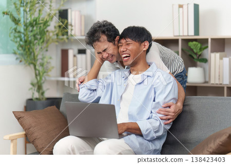 LGBTQ couple laughing together while using a laptop LGBTQ couple laughing together while using a laptop 138423403