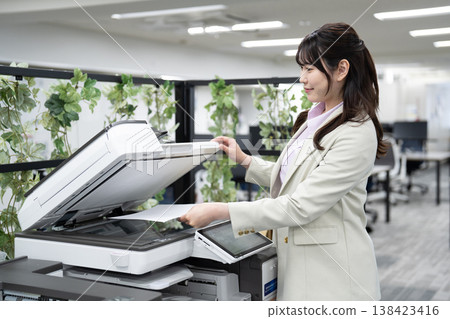一名女員工在辦公室操作多功能印表機。 一名女員工在辦公室操作多功能印表機。 138423416