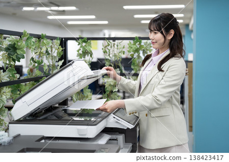 A female employee operating a multifunction printer in the office. 138423417