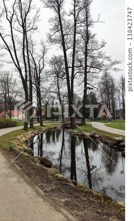 Sunny city park with a bare trees and a deep pond in early spring. Ideal for travel imagery, recreation visuals, and design projects. 138423747