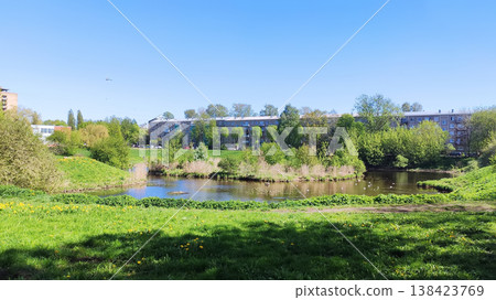 Peaceful riverside scene with sunlight reflecting on water and fresh foliage. Works well for relaxation visuals, travel content, and nature in the city. 138423769