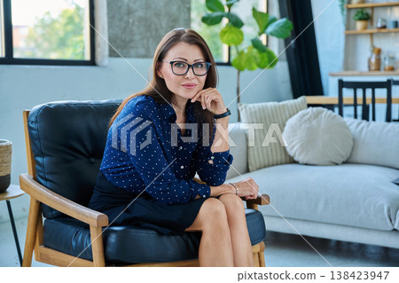 Portrait of beautiful serious middle-aged woman sitting in chair Portrait of beautiful serious middle-aged woman sitting in chair 138423947