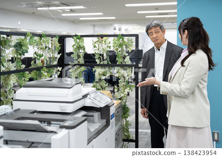 A female employee and her male supervisor explain how to use the multifunction printer in the office. A female employee and her male supervisor explain how to use the multifunction printer in the office. 138423954