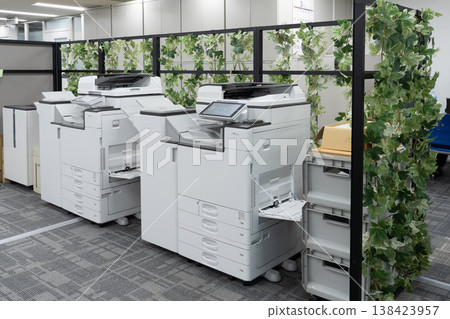 Copy machines and office greenery lined up next to the partition. 138423957